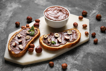 Board of bread with chocolate paste and hazelnuts on black background
