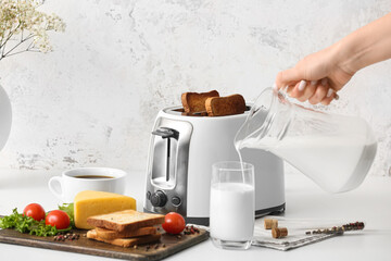 Woman pouring milk into glass near toaster in kitchen