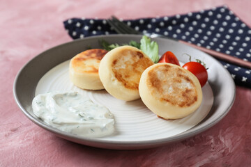 Plate with tasty cottage cheese pancakes, sauce and tomato on pink background, closeup