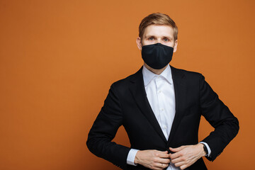Man wearing black FFP2 face mask while standing against orange background. Time to upgrade masks as coronavirus variants emerge. Double masking Covid-19 protection. FFP2 respirator for public health