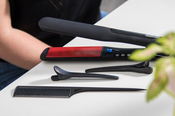 Black hair straightener and curler sitting on white table with hair tools