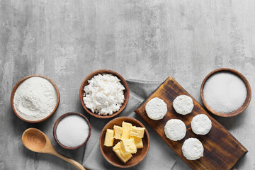 Wooden board with uncooked cottage cheese pancakes and ingredients on grey background