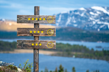review stars and faces emoji engraved on wooden signpost outdoors in nature during blue hour.