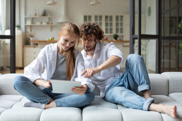 Young couple with digital tablet on cozy sofa, online shopping together at home