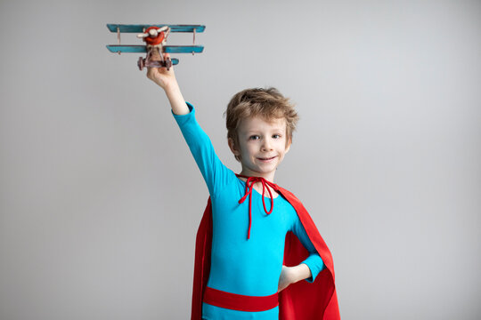 Little superhero boy in a red cape plays with an airplane. Happy smiling child. Success, motivation and travel.