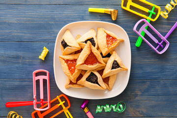 Hamantaschen cookies and rattles for Purim holiday on color wooden background