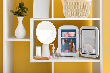 Shelf unit with small refrigerator and cosmetic products near color wall in room