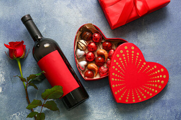 Heart shaped box with tasty chocolate candies, rose and bottle of wine on blue background