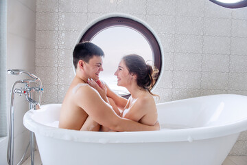 Close-up portrait of couple face to face in bubble bath at round window overlooking the sea. Man...