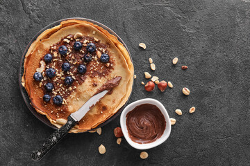 Plate of tasty thin pancakes with chocolate paste, blueberries and nuts on black background
