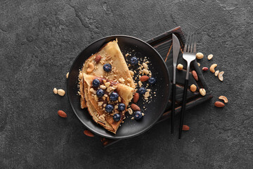 Plate of tasty thin pancakes with chocolate paste, blueberries and nuts on black background