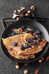 Plate of tasty thin pancakes with chocolate paste, blueberries and nuts on black background