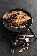 Plate of tasty thin pancakes with chocolate paste, blueberries and nuts on black background