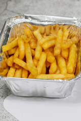 French fries in a foil takeaway tray with lid. On a concrete background