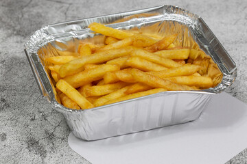 French fries in a foil takeaway tray with lid. On a concrete background