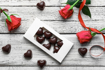 Box with tasty heart-shaped candies and flowers on light wooden background