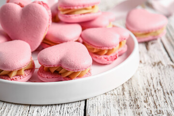Plate with tasty heart-shaped macaroons on white wooden background, closeup