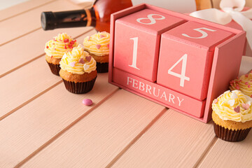 Calendar with date of Valentines Day and tasty cupcakes on pink wooden background