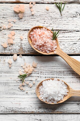 Spoons with sea salt on light wooden background, closeup