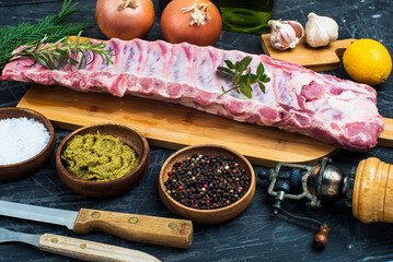 Ribs of a young pig on a wooden board with rosemary, pepper and spices.