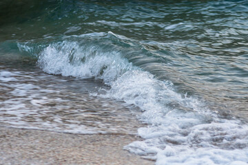 Close-up photo of a sea wave near a sandy shore, blurred to give the effect of movement