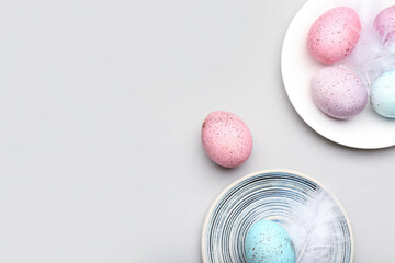 Plates with beautiful Easter eggs and feathers on grey background