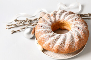 Plate with tasty Easter cake, willow branches and eggs on light background