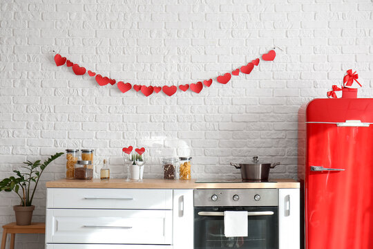 Stylish red refrigerator and counters near white brick wall in kitchen decorated for Valentine's day celebration