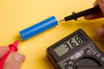 battery with volt calculator, voltmeter in the hands of a man, red positive pole, black negative...