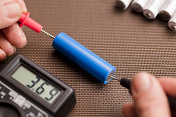 battery with volt calculator, voltmeter in the hands of a man, red positive pole, black negative...