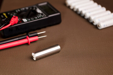 battery with volt meter, red positive pole, black negative pole, on yellow work table