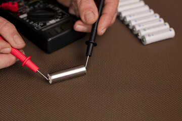 battery with volt calculator, voltmeter in the hands of a man, red positive pole, black negative...