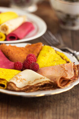 Multicolored flat pancakes on a plate decorated with raspberries. Original food pancakes on Maslyanitsa
