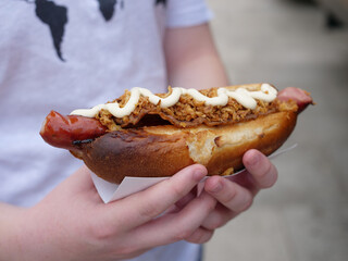 Young man holds a large hot dog with ketchup and mayonnaise in his hands