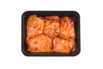Raw marinated chicken thighs in red sauce in a tray for a supermarket, on a white isolated background.Raw chicken marinated.Retail.Isolated object, copy space.Chicken semi-cooked thighs. Top of view.