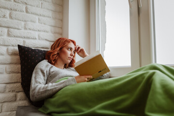 Obraz premium The girl with the orange hair is lying in bed and thinking