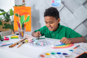 Naklejka premium Boy sitting at table pushing tubes of paint