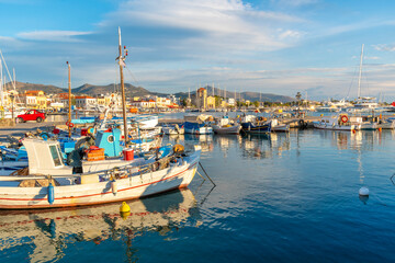 Fototapeta na wymiar Colorful fishing boats line the harbor of the Greek island of Aegina, Greece at dusk, with the waterfront promenade and village in view. 