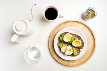 Flat lay avocado toast with eggs on dark bread, black coffee and glass of water on white background. High quality photo