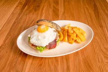 Hamburger with corned beef, fried egg with yolk on top, lettuce and garnish of homemade fries