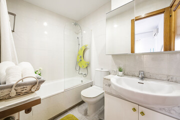 Bathroom with white furniture, white porcelain toilets, shower with glass partition and rolled...