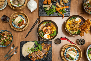 Set of asian food dishes with lots of ramen, bao bread, crispy duck, soy sauce, gyozas, spring and vietnamese rolls and boiled shrimp