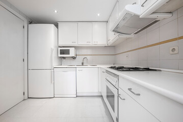 Conventional kitchen with white furniture and appliances, gray handles and white countertop with...
