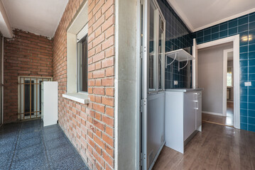 Conventional kitchen with white cabinets, gray countertop and small square blue tiles on the walls and closed terrace with brown brick walls