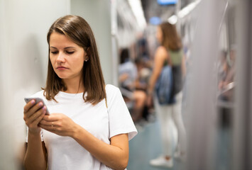 Young woman browsing and typing messages on phone in subway car
