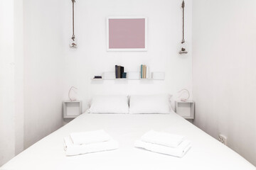 Fototapeta na wymiar Bedroom with king size bed, white led lamps, white cushions and pillows and matching towels
