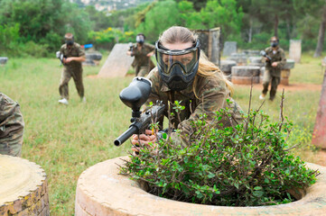 Fototapeta premium Female paintball player in protective mask with ammunition and gun on paintball field