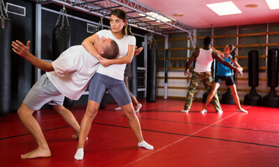 Fototapeta premium Woman practising neck grabbing self-protective move with man during group training. African-american man sparring with woman in background.