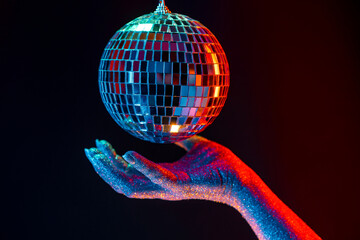 Glitter female hand holding spinning disco mirror ball under neon. Glossy silver sphere reflecting...
