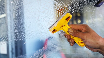 Razor handle to clean the windshield. Workers use a yellow scraper to scrape glue and dirt off the glass to clean before installing a new window film with a copy area. Selective focus - obrazy, fototapety, plakaty